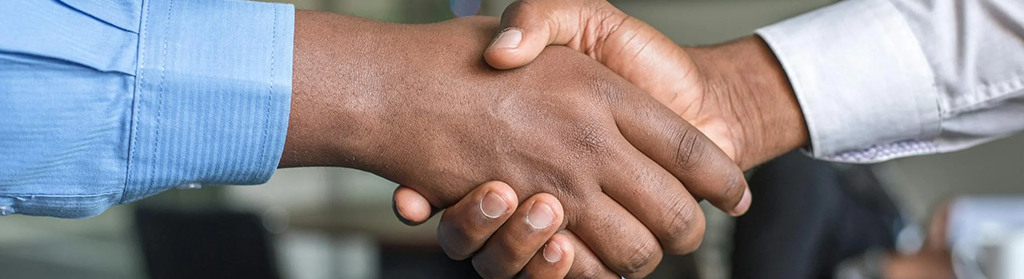 Two hands shaking - The left one has a blue sleeve, and the right one has a white sleeve.